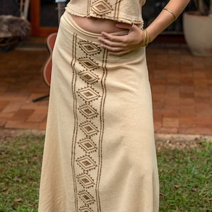 May include: A beige skirt with a brown geometric pattern. The skirt is made of a lightweight fabric and has a flowy silhouette.