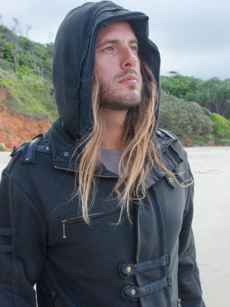 May include: Dark gray hooded jacket with a zipper closure and multiple decorative straps. The jacket has a high collar and a hood. The person in the image has long, light brown hair.