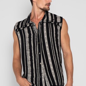 May include: A sleeveless button-up shirt with a black and white striped pattern. The shirt has a collar and a button-up front.