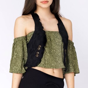 May include: A black sleeveless vest with a ruffled neckline and four gold buttons. The vest is worn over a green floral print top.