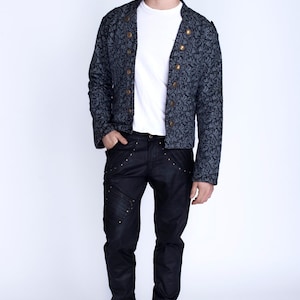 Puede incluir: Un hombre con una chaqueta azul oscuro con estampado y botones dorados, pantalones vaqueros negros con costuras decorativas y zapatos negros.