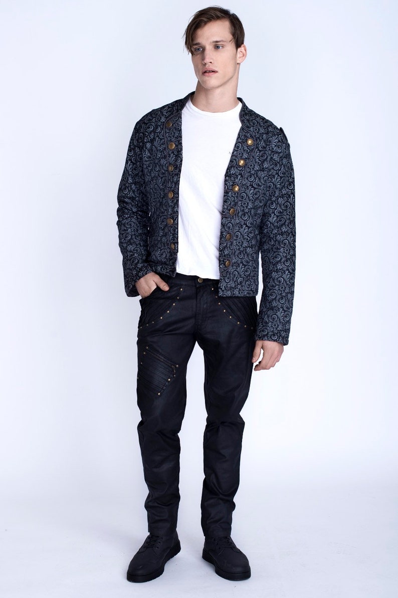 Puede incluir: Un hombre con una chaqueta azul oscuro con estampado y botones dorados, pantalones vaqueros negros con costuras decorativas y zapatos negros.