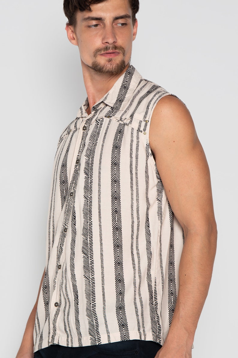 May include: A sleeveless button-up shirt with a white background and black chevron pattern. The shirt has a collared neckline and a button closure.