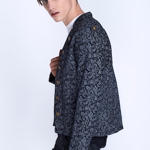 Puede incluir: Una chaqueta azul con estampado y botones dorados. La chaqueta tiene un cuello alto y mangas largas.
