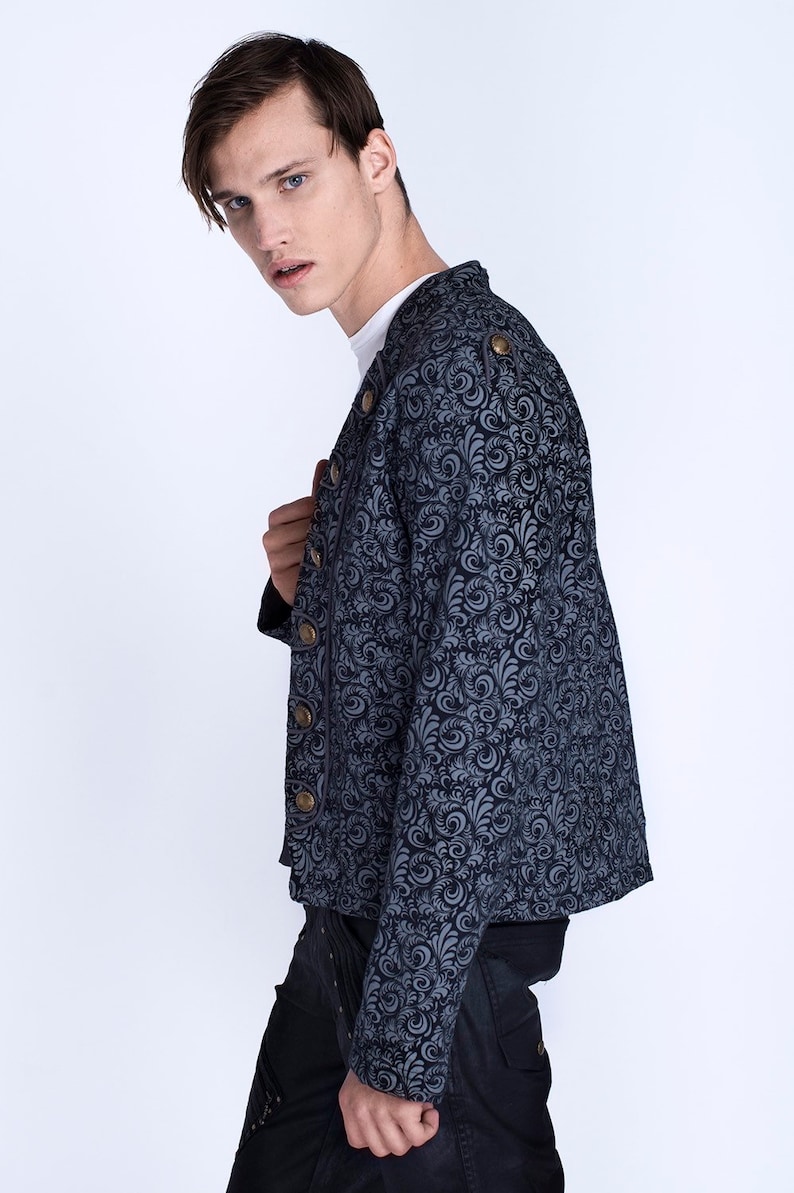 Puede incluir: Una chaqueta azul con estampado y botones dorados. La chaqueta tiene un cuello alto y mangas largas.