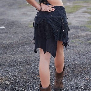 May include: A black asymmetrical skirt with multiple layers and textures. The skirt features a patterned top section, a lace middle layer, and a jagged hemline. Small silver studs are visible. The skirt is paired with brown boots.