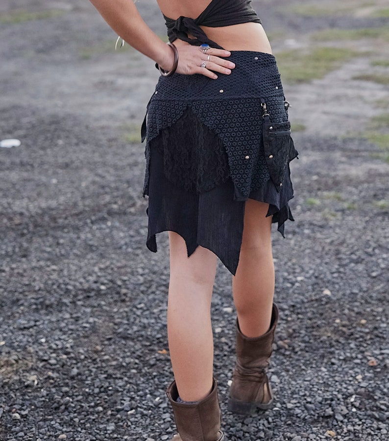 May include: A black asymmetrical skirt with multiple layers and textures. The skirt features a patterned top section, a lace middle layer, and a jagged hemline. Small silver studs are visible. The skirt is paired with brown boots.