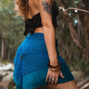 May include: A black halter top and a blue skirt with a lace overlay. The skirt is layered, with a teal underlay and a decorative tassel. The image shows a close-up of the skirt and top, with a natural background.