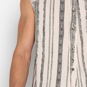 May include: A sleeveless button-up shirt with a white background and black chevron stripes. The shirt has a pointed collar and a button-up front.