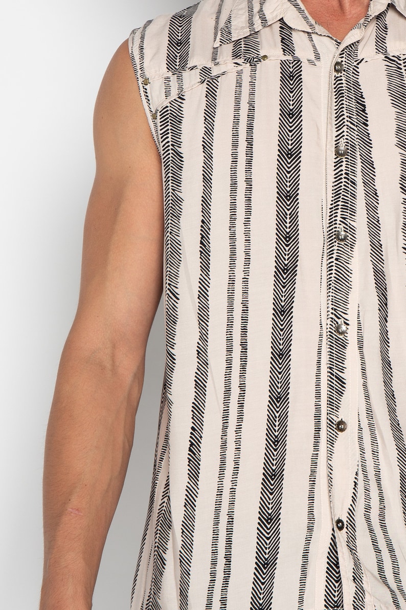 May include: A sleeveless button-up shirt with a white background and black chevron stripes. The shirt has a pointed collar and a button-up front.