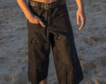 May include: Black and white striped culottes with a matching belt. The culottes have a wide leg and a high waist. The belt is black leather with silver studs. The person is standing on a sandy beach.
