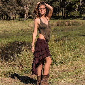 May include: A woman wearing a brown and green halter top with a brown ruffled skirt and brown boots. She is standing in a grassy field.