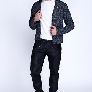 Puede incluir: Un hombre con una chaqueta de patr&oacute;n azul oscuro con botones dorados, pantalones vaqueros negros con detalles dorados y zapatos negros.