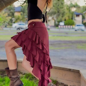 May include: A woman wearing a black halter top and a burgundy ruffled skirt. She is standing on a concrete surface with green grass in the foreground.