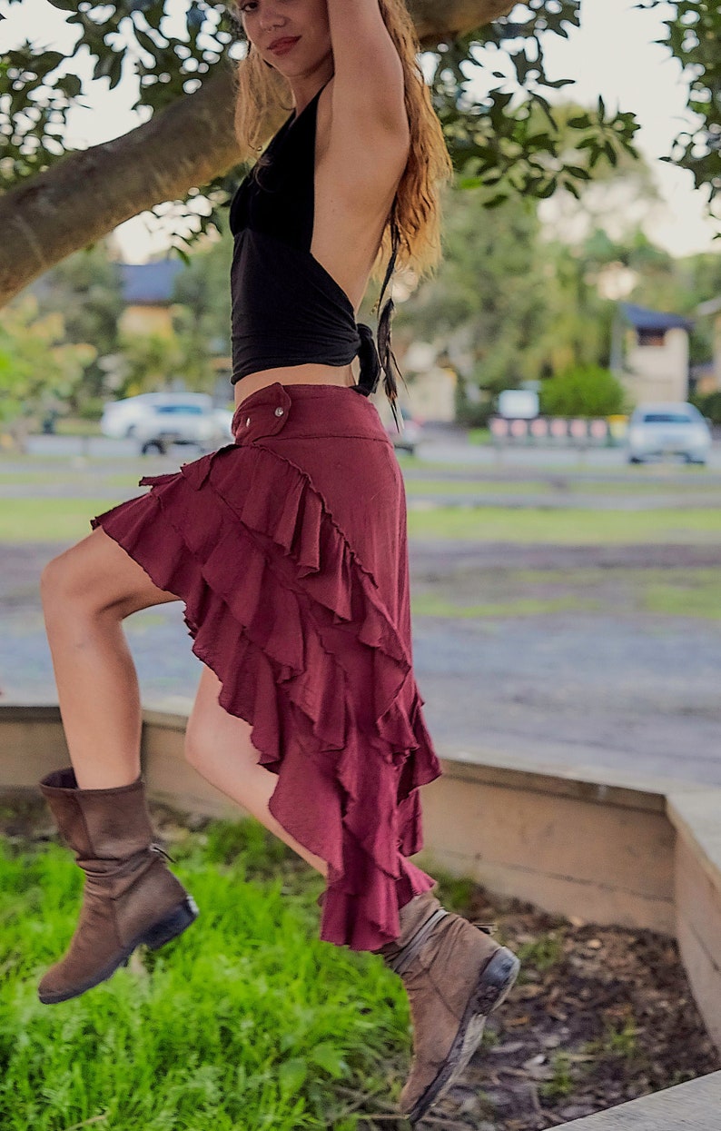 May include: A woman wearing a black halter top and a burgundy ruffled skirt. She is standing on a concrete surface with green grass in the foreground.