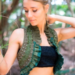 May include: An olive green sleeveless vest featuring a high ruffled collar, dark green lace trim along the front edges, and a vertical row of silver-toned metal studs on the chest. The garment is worn over a black strapless lace top.
