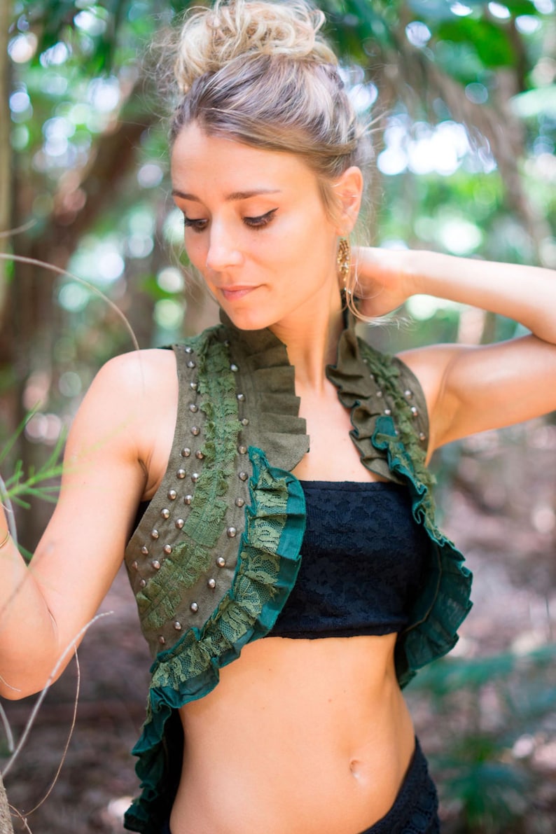 May include: An olive green sleeveless vest featuring a high ruffled collar, dark green lace trim along the front edges, and a vertical row of silver-toned metal studs on the chest. The garment is worn over a black strapless lace top.