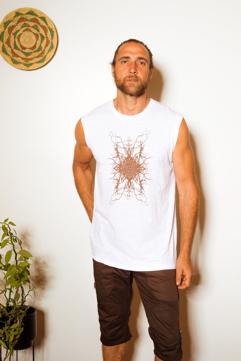 May include: A white sleeveless shirt with a brown geometric design. The shirt is worn by a person with brown hair and a beard. The person is wearing brown shorts.