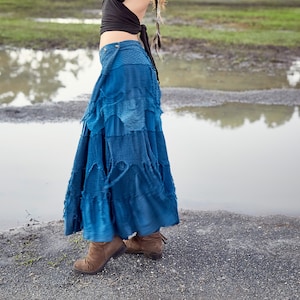 Peut inclure: Une femme portant une jupe en jean bleu à plusieurs couches et un ourlet à volants. La jupe est faite de denim recyclé et a un look unique et artisanal.