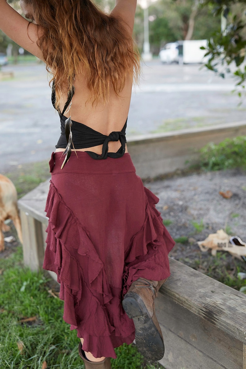 May include: A woman wearing a black halter top with a feather detail and a burgundy ruffled skirt. She is wearing brown boots and has her back to the camera.