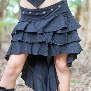 May include: A black, tiered skirt with a high-low hemline. The skirt has a wide waistband with silver buttons and a ruffled bottom.