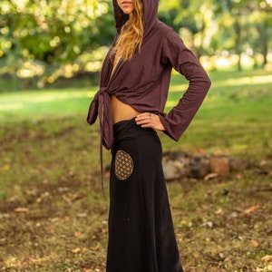 May include: A woman wearing a long, black skirt with a gold flower of life design. She is also wearing a purple hooded top tied at the waist.