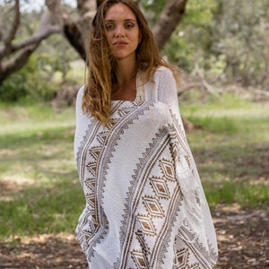 May include: A woman wearing a white and brown patterned shawl with fringe. The shawl has a geometric design and is draped over her shoulders.
