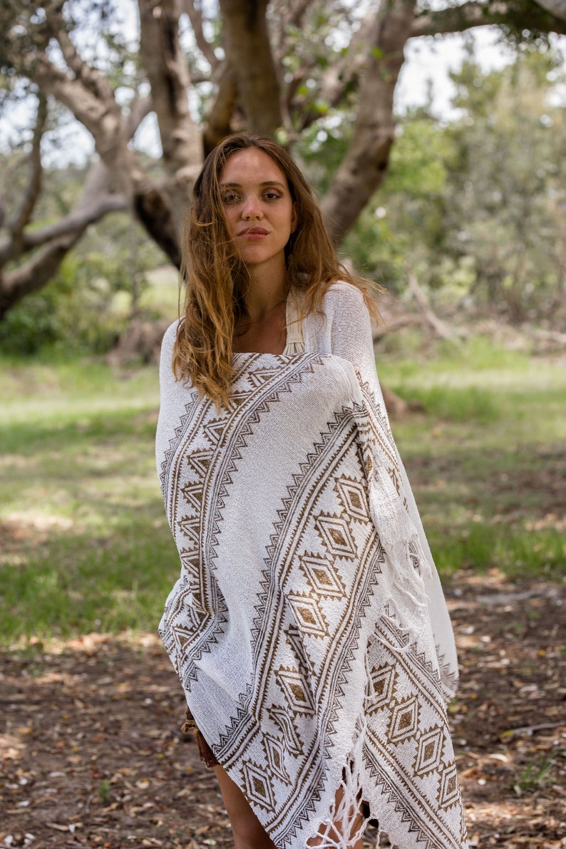 May include: A woman wearing a white and brown patterned shawl with fringe. The shawl has a geometric design and is draped over her shoulders.