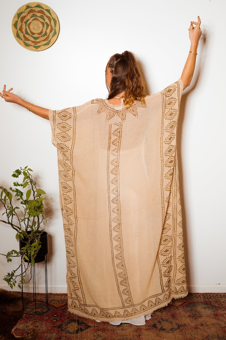 Puede incluir: Una larga kaft&aacute;n beige y transparente con un patr&oacute;n geom&eacute;trico marr&oacute;n. La kaft&aacute;n tiene un corte holgado y fluido, ideal para superponer.