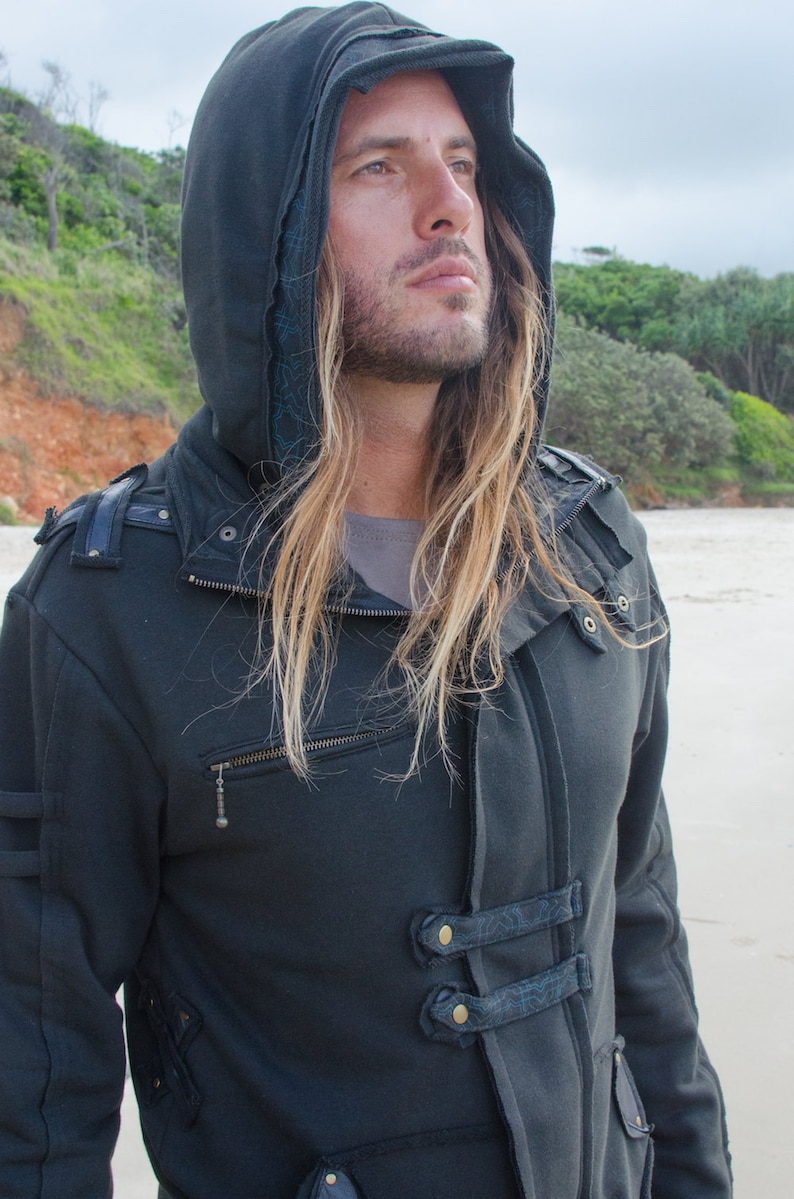 May include: Dark gray hooded jacket with a zipper closure and decorative straps. The jacket features a hood with a brim and is made of a thick, textured fabric. The jacket has a unique design with multiple pockets and decorative elements.