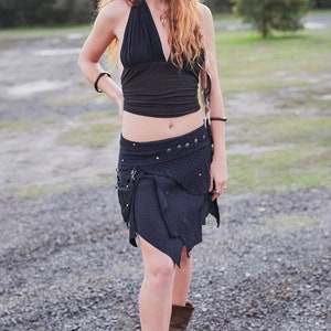 May include: A black halter top and a dark blue asymmetrical skirt with decorative studs and pockets. The skirt is paired with brown boots. The outfit is suitable for a bohemian or alternative style.