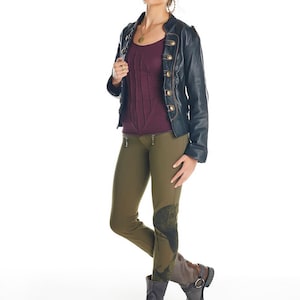 May include: A woman wearing a black leather jacket with gold buttons, a burgundy top, and olive green pants with a graphic print. She is wearing brown boots with buckles.