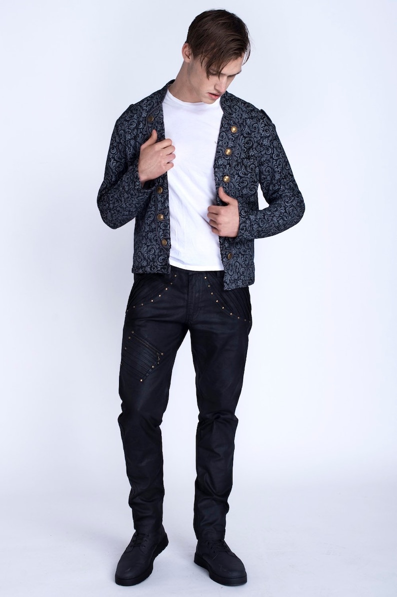 Puede incluir: Un hombre con una chaqueta azul oscuro con estampado y botones dorados, pantalones vaqueros negros con costuras decorativas y zapatos negros.