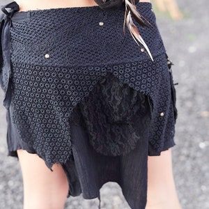 May include: Black crochet skirt with lace and fabric details. The skirt has a unique, asymmetrical design with a layered look. Embellished with small silver studs and feathers, it's a bohemian style piece.