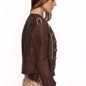 May include: A brown leather jacket with a cream trim and gold buttons. The jacket has a cropped length and a fitted silhouette.