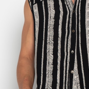 May include: A sleeveless button-up shirt with a black and white chevron pattern. The shirt has a classic collar and a button-up front.