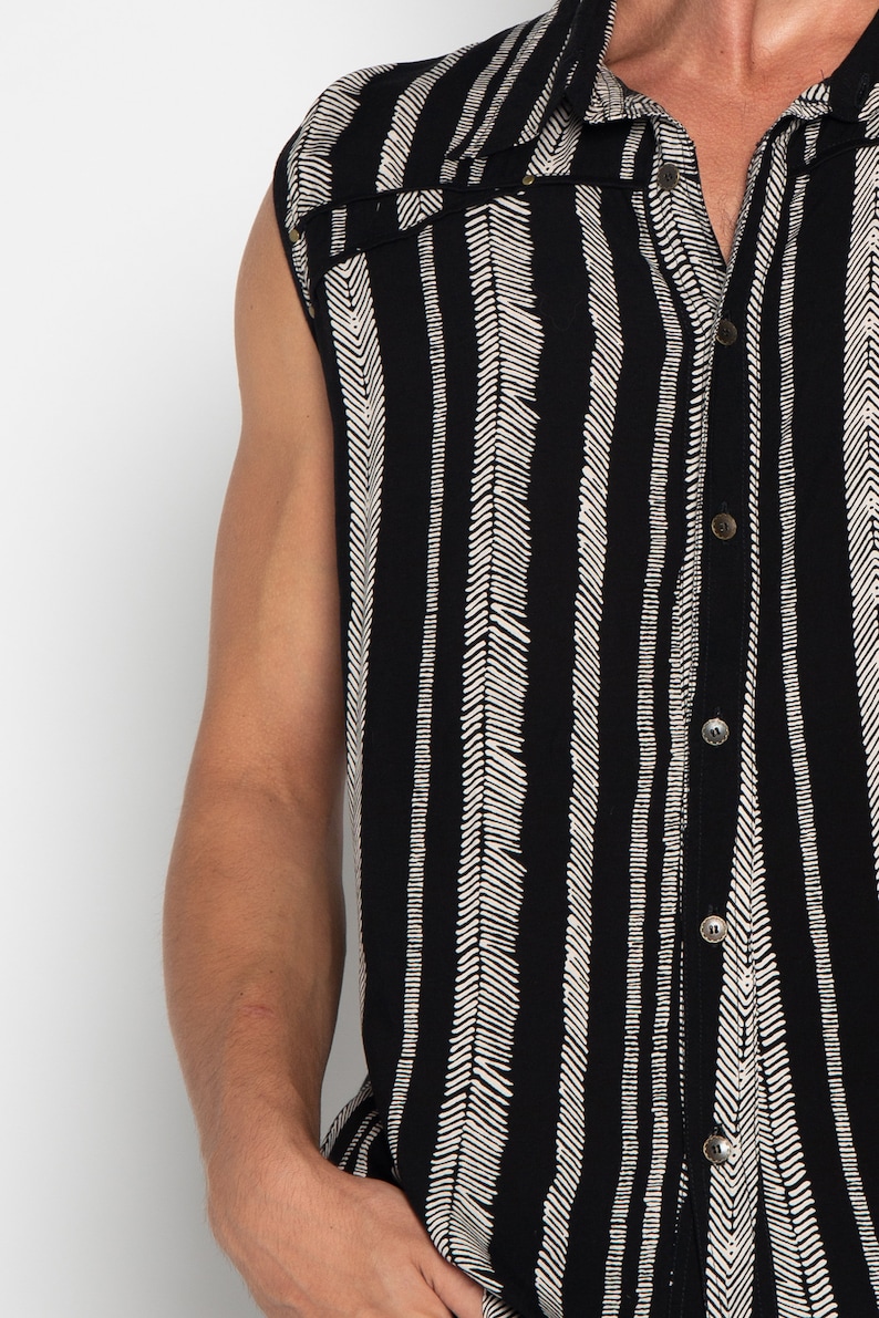 May include: A sleeveless button-up shirt with a black and white chevron pattern. The shirt has a classic collar and a button-up front.