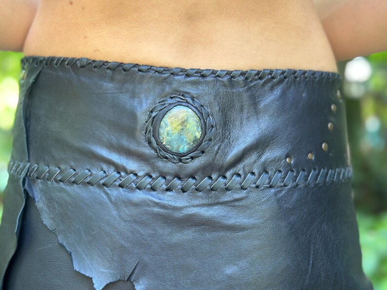 May include: A black leather belt with a braided design and a circular, green gemstone accent.