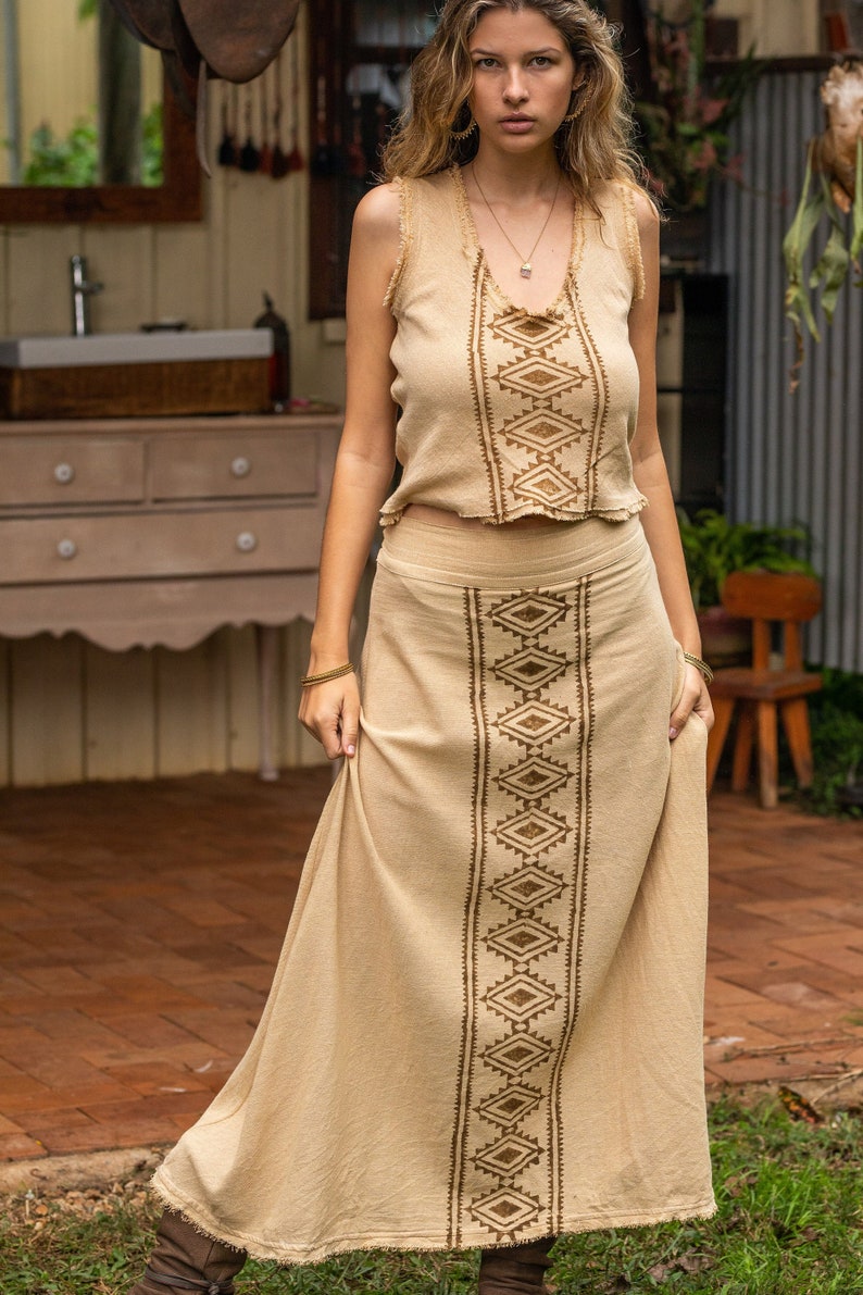 May include: A beige sleeveless top with a brown geometric pattern and a matching beige maxi skirt with a brown geometric pattern. The skirt has a raw hem.