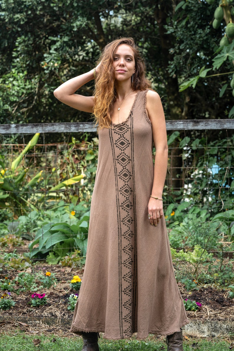 May include: A brown sleeveless maxi dress with a geometric pattern in black. The dress has a relaxed fit and a frayed hem.