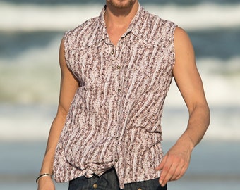 May include: A man wearing a sleeveless, patterned button-down shirt with a light brown and white color scheme. He is wearing dark blue jeans with gold buttons.