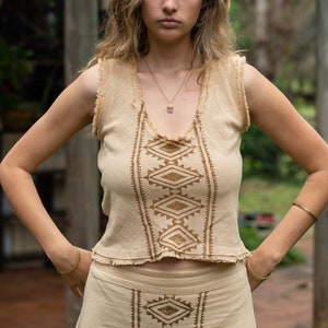 May include: A woman wearing a beige sleeveless top and skirt with a brown geometric pattern. The top and skirt are made of a lightweight fabric and have a relaxed fit.