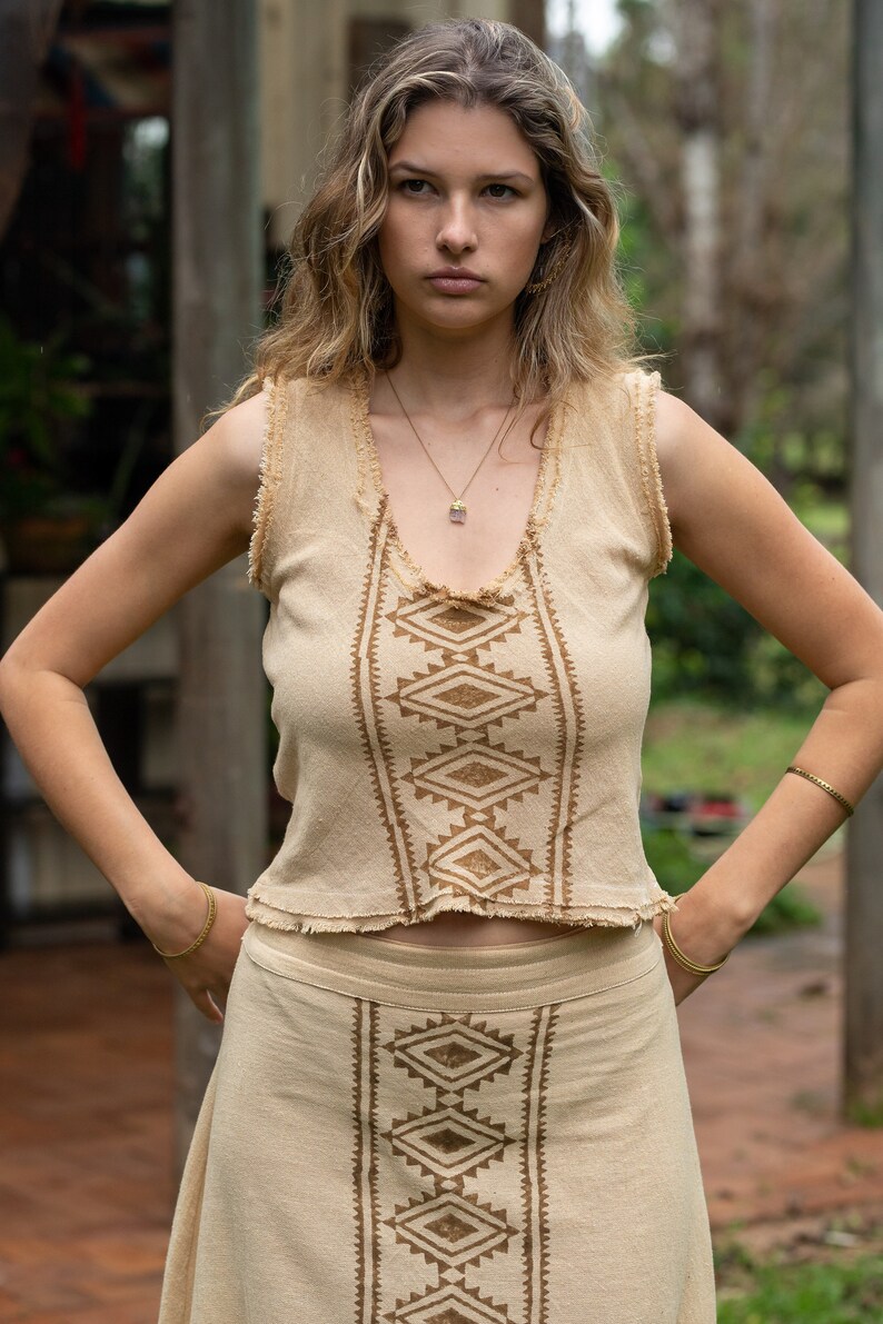 May include: A woman wearing a beige sleeveless top and skirt with a brown geometric pattern. The top and skirt are made of a lightweight fabric and have a relaxed fit.