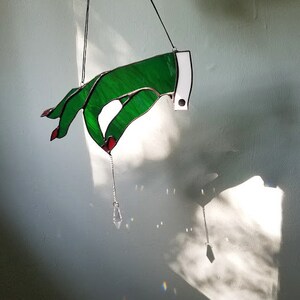 May include: A stained glass hand with red fingernails, holding a crystal prism. The hand is green and white and is hanging from the ceiling.