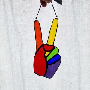 May include: A stained glass peace sign window hanging. The peace sign is made of red, orange, yellow, green, blue, and purple glass.