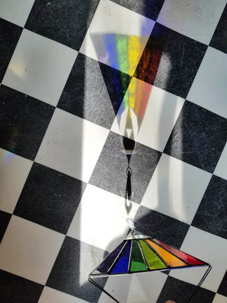 May include: A rainbow stained glass prism hanging from a black metal chain on a black and white checkered background.