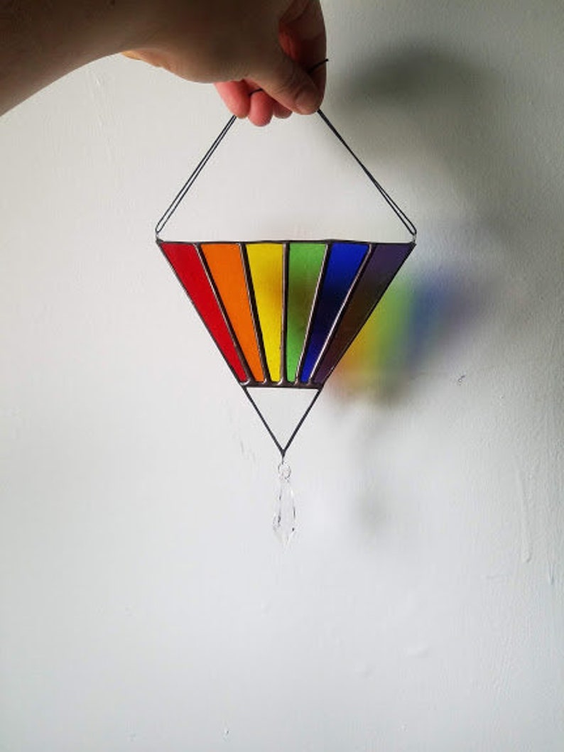 May include: A rainbow stained glass suncatcher with a crystal prism hanging from the bottom. The suncatcher is shaped like a diamond and is made of red, orange, yellow, green, blue, indigo, and violet glass.