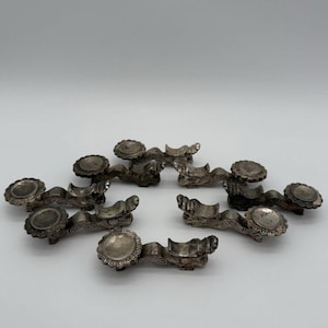 May include: A set of six silver-toned metal chopstick rests, each featuring a detailed dragon-shaped body with an elongated tail and a circular, scalloped-edge platform at one end for holding chopsticks securely in place.