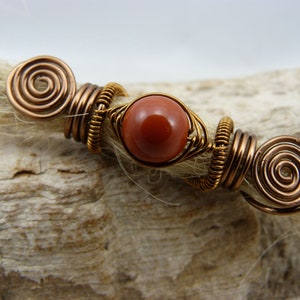 May include: Copper wire dreadlock beads with a red gemstone in the center.