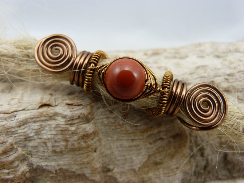 May include: Copper wire dreadlock beads with a red gemstone in the center.
